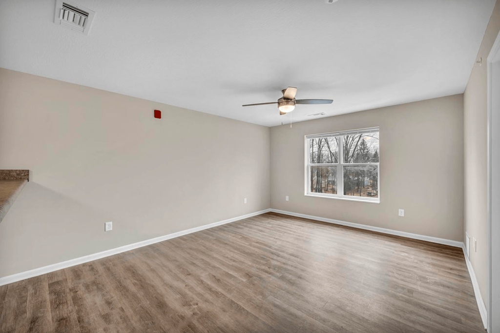 an empty living room with a ceiling fan and a window