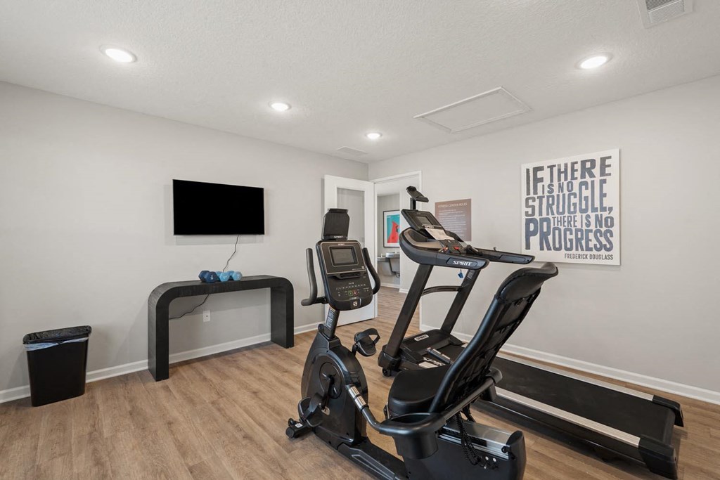 A gym room with a treadmill, exercise bike, and a flat screen TV.