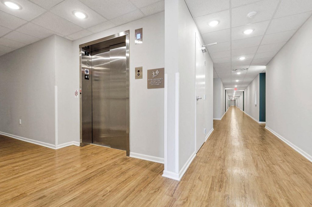 a long hallway with white walls and wood floors and an elevator