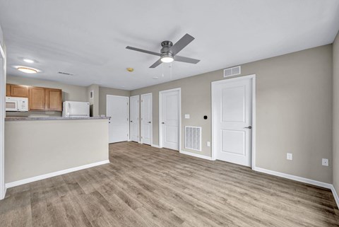 A room with a ceiling fan and a kitchen area with cabinets and a fridge.