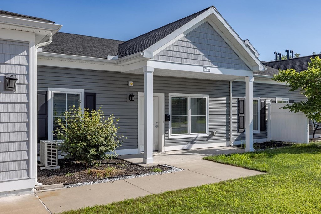 the front of a gray house with a sidewalk and grass