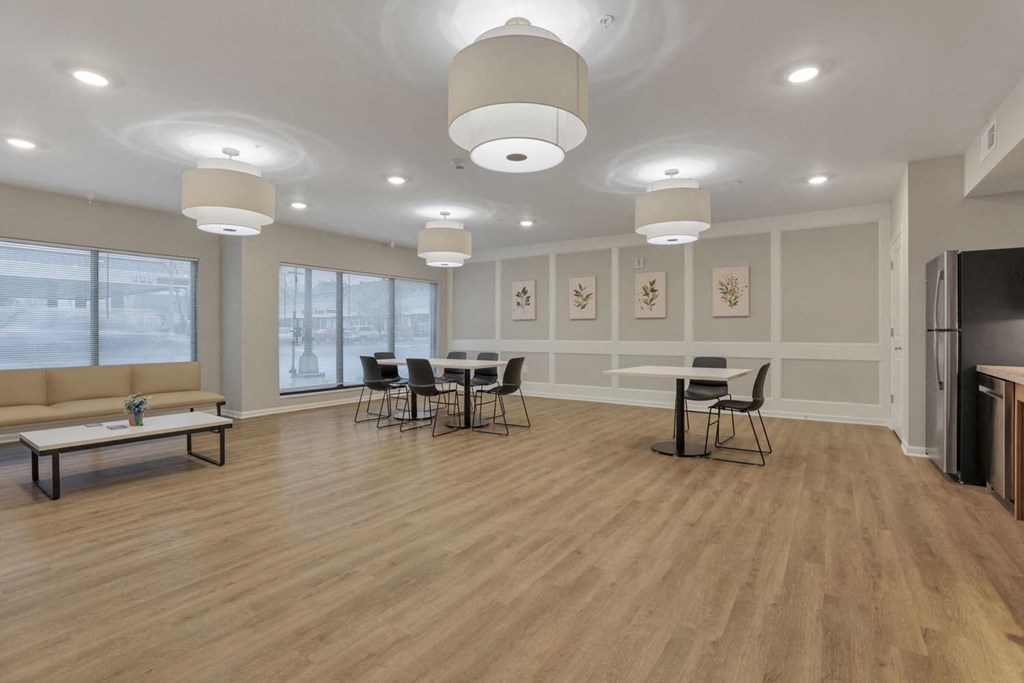 an empty living room with tables and chairs and a refrigerator