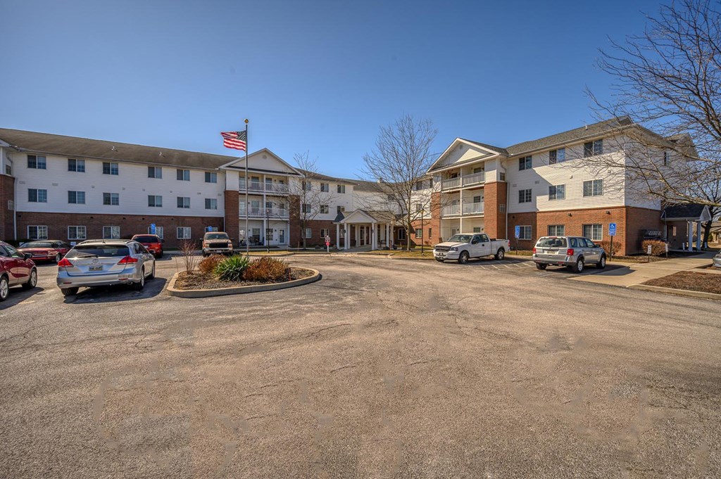 A parking lot in front of a multi-story apartment building with cars parked.