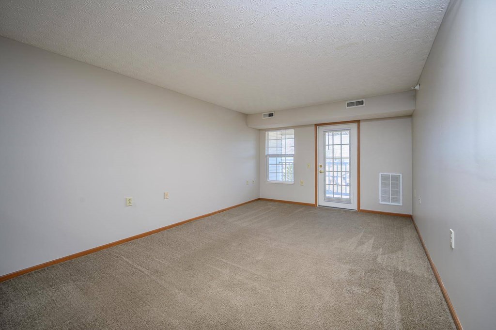 A room with a carpeted floor and two windows.
