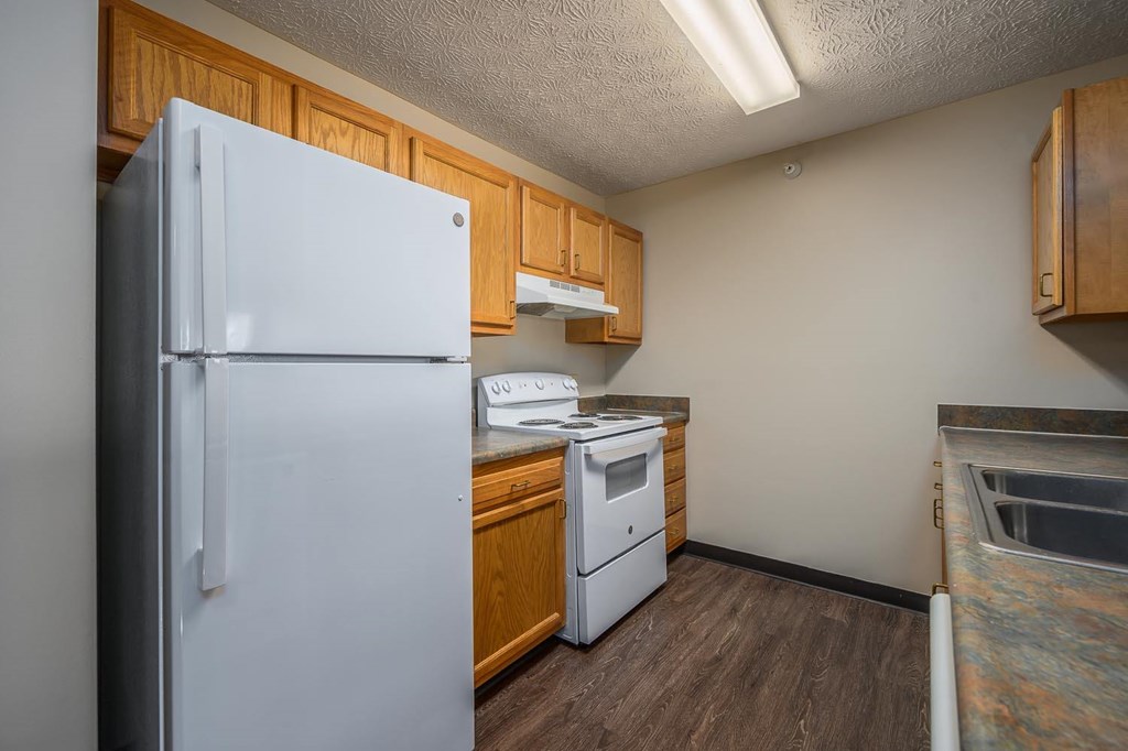 A white refrigerator stands in a kitchen with wooden cabinets and a white dishwasher.