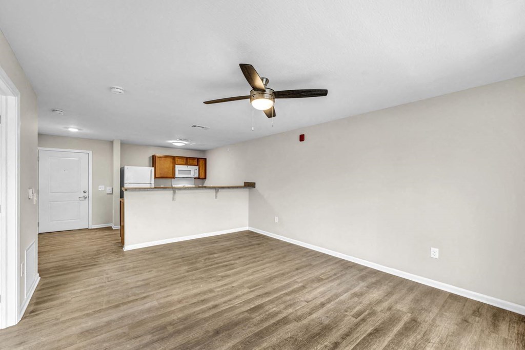 an empty living room with a ceiling fan and a kitchen