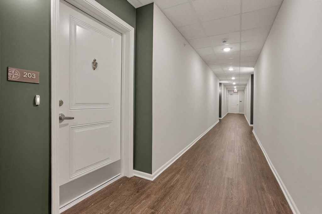 a long hallway with white doors and green walls and wooden floors