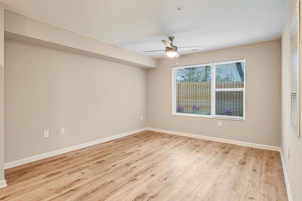 A room with wooden flooring and a window with a view of a fence.