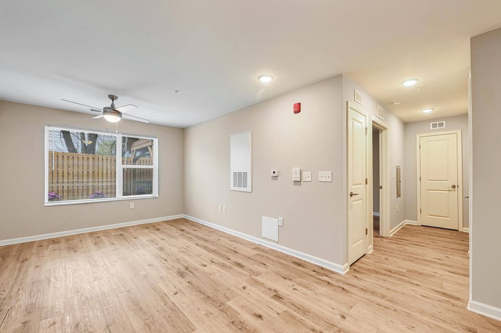 A room with a ceiling fan and a window with a view of a fence and trees.