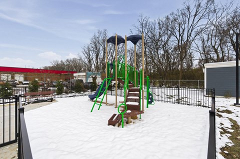 A playground with a green slide and a red building in the background.