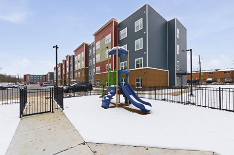 A playground with a slide and a fence in front of apartment buildings.