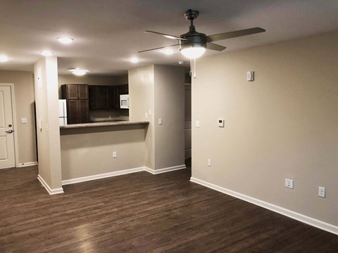 a empty living room with a ceiling fan and a kitchen