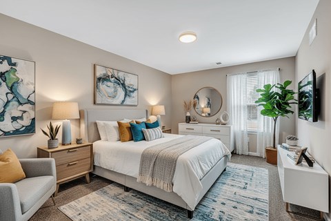A bedroom with a large bed, a grey couch, and a painting on the wall.