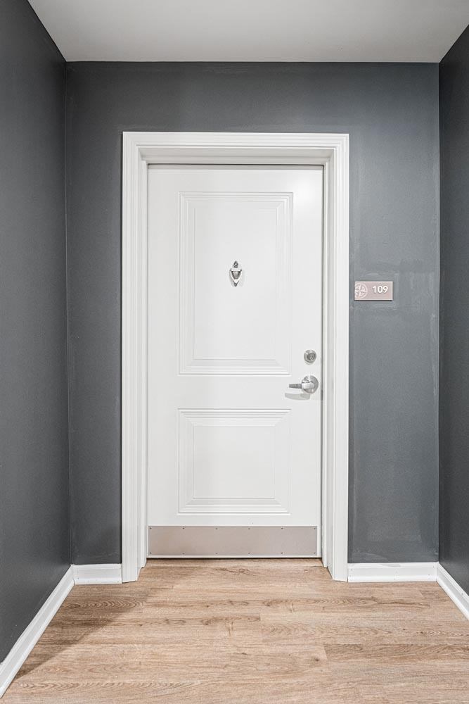 A white door with a handle and a doorknob is in a room with grey walls.