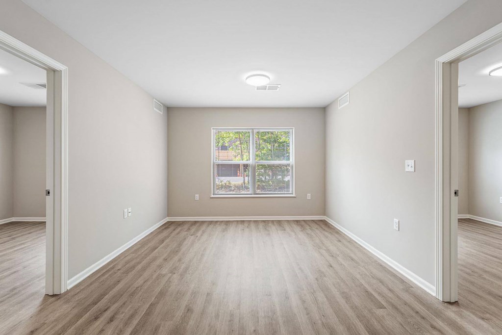 A spacious room with light wood flooring and a large window.