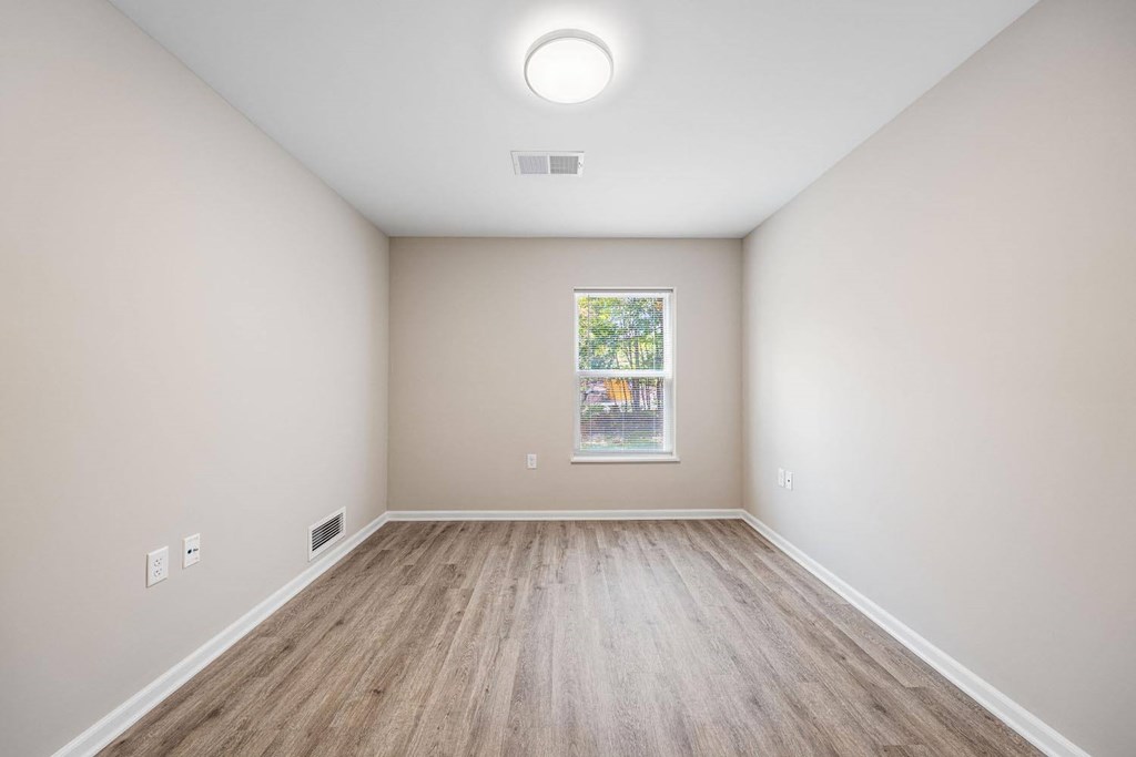 A room with wooden flooring and a window showing a view of trees.