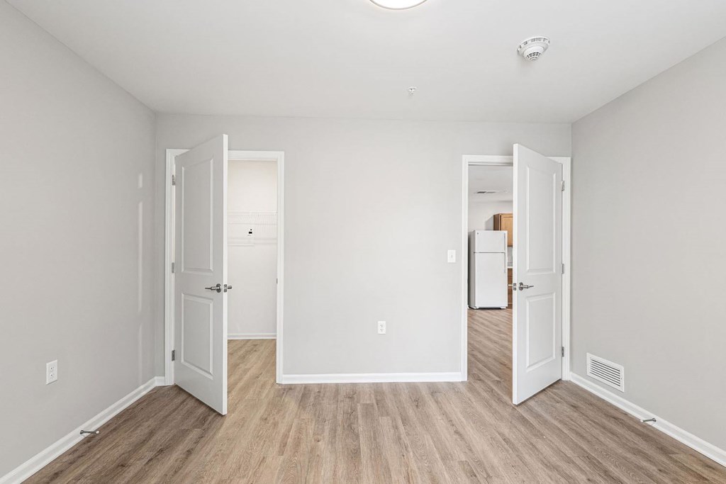 A room with white walls and wood flooring with two open doors.