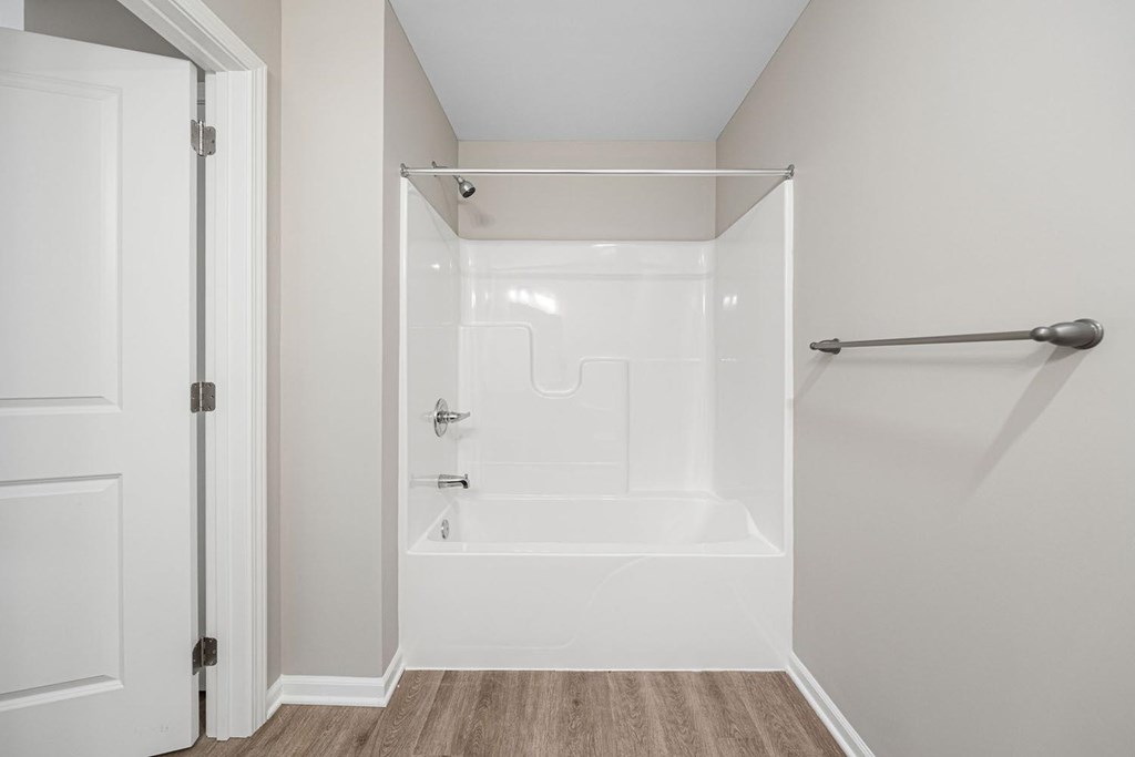 A white bathroom with a walk-in shower and a door open to a hallway.