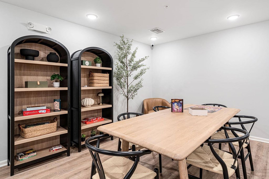 A room with a wooden table, chairs, and a bookshelf with various items.