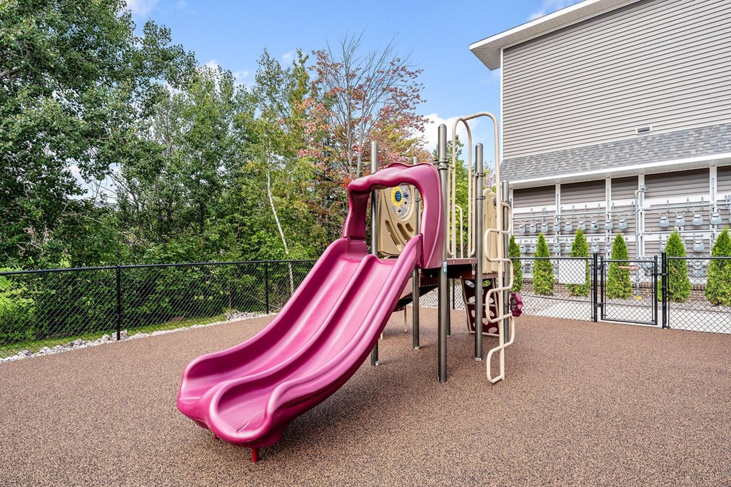 A pink slide in a playground with a wooden top.