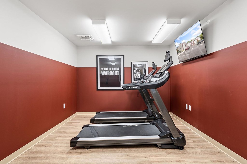 A treadmill in a room with a red wall and a television.