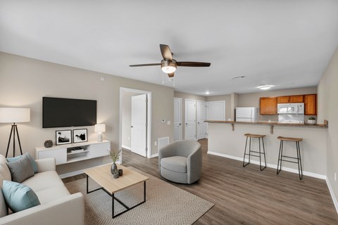 A living room with a white couch, a grey armchair, a wooden coffee table, and a flat-screen TV mounted on the wall.