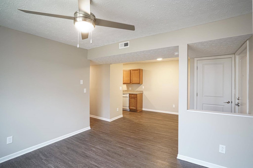 an empty living room with a ceiling fan and a kitchen