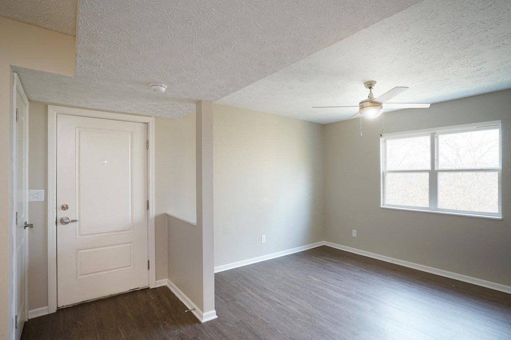 an empty living room with a white door and a ceiling fan