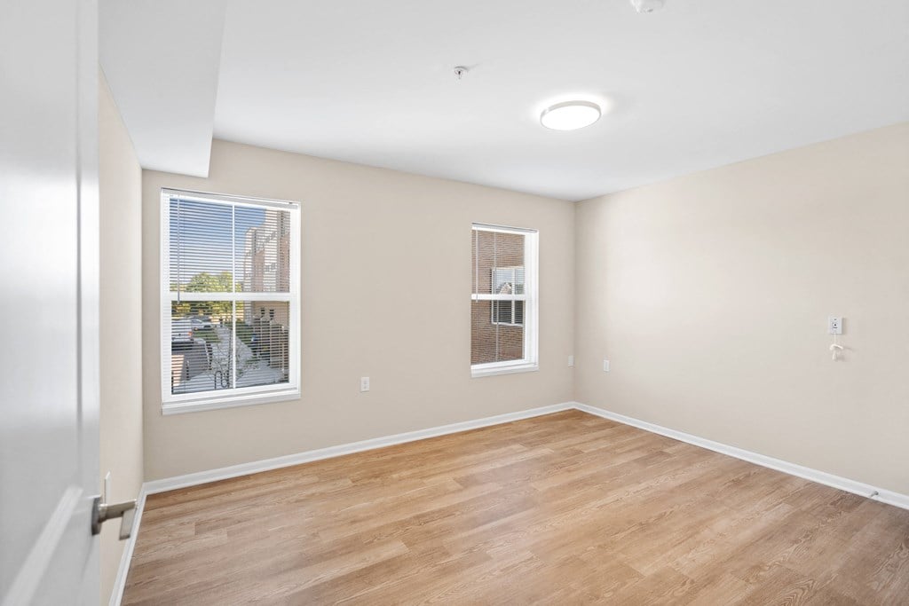an empty living room with wood flooring and two windows
