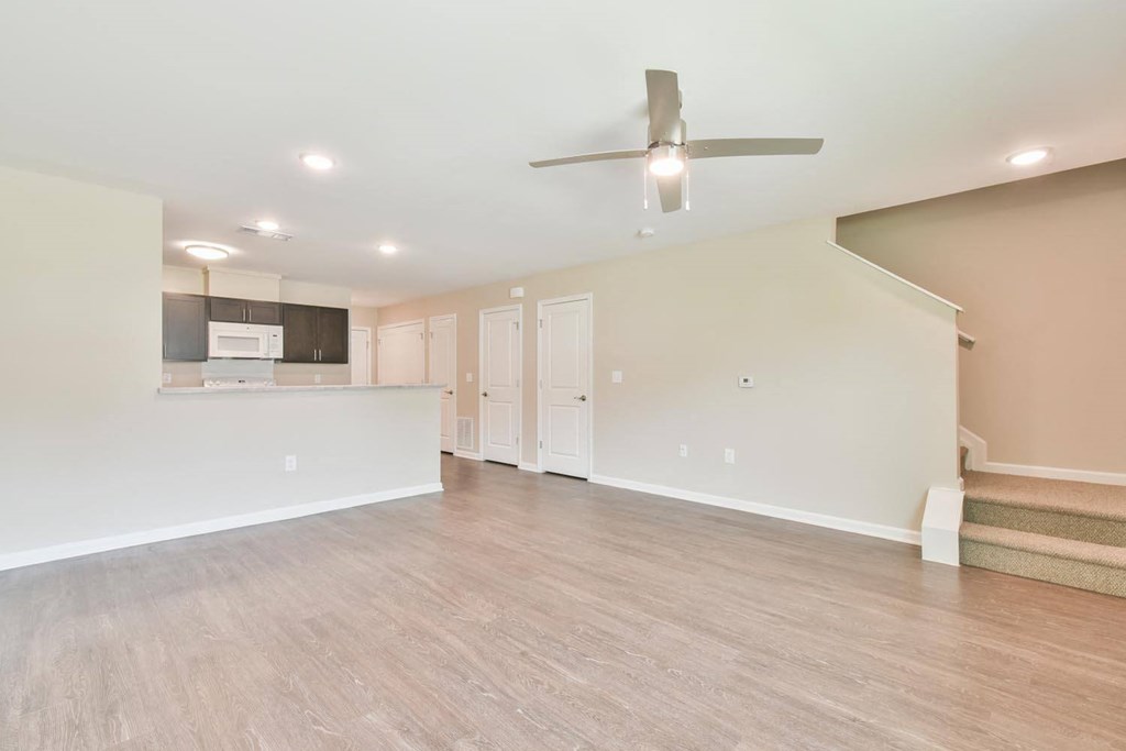 a living room with a ceiling fan and a kitchen in the background