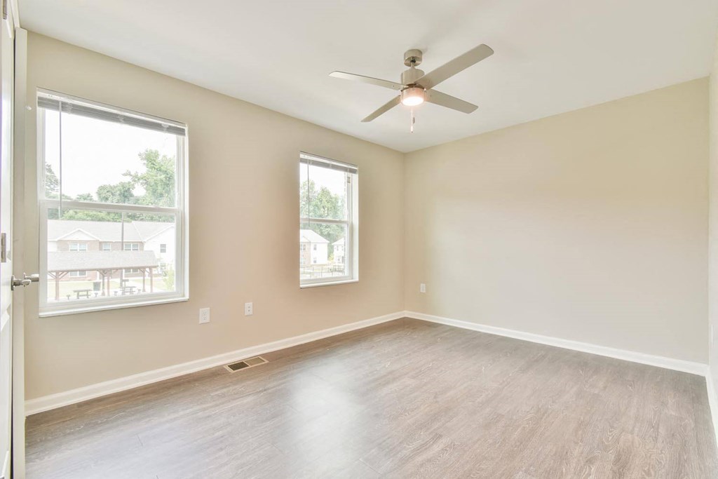 an empty bedroom with a ceiling fan and two windows