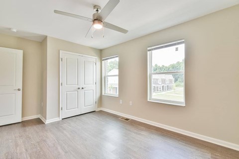 an empty bedroom with a ceiling fan and two windows