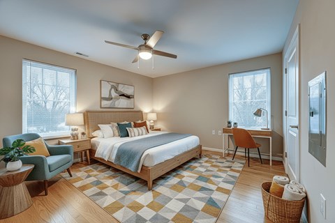 A bedroom with a bed, desk, chair, and a ceiling fan.