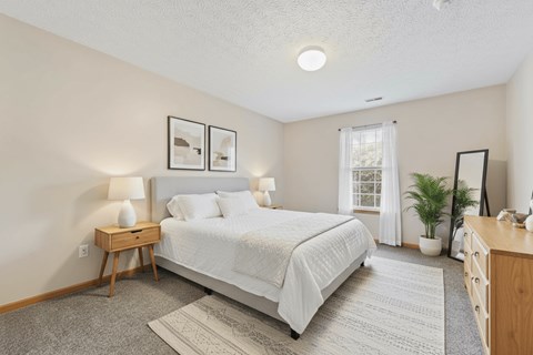 A bedroom with a bed, nightstand, and a window.