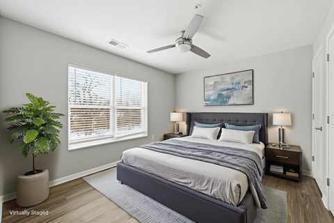 A bedroom with a large bed, a potted plant, and a ceiling fan.