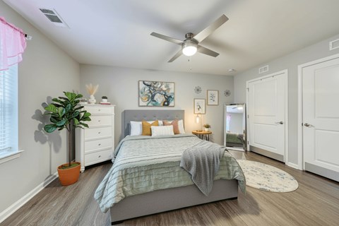 A bedroom with a bed, a ceiling fan, and a potted plant.