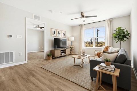 A living room with a grey couch, a wooden coffee table, a flat screen TV, and a ceiling fan.