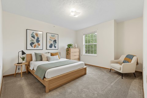 A bedroom with a bed, chair, and two framed pictures on the wall.