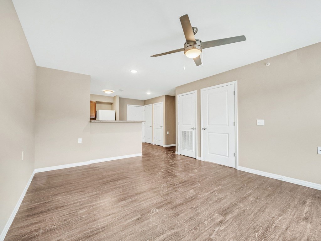 an empty living room with a ceiling fan and a kitchen