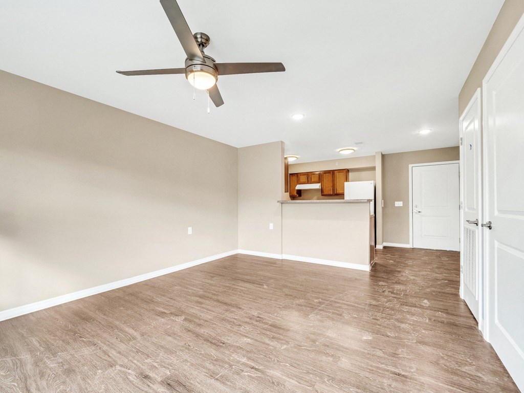 an empty living room with a ceiling fan and a kitchen