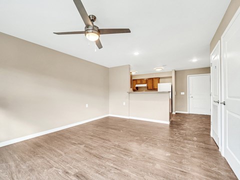 an empty living room with a ceiling fan and a kitchen