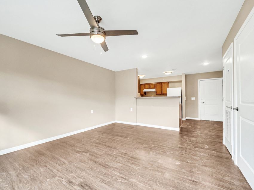 an empty living room with a ceiling fan and a kitchen