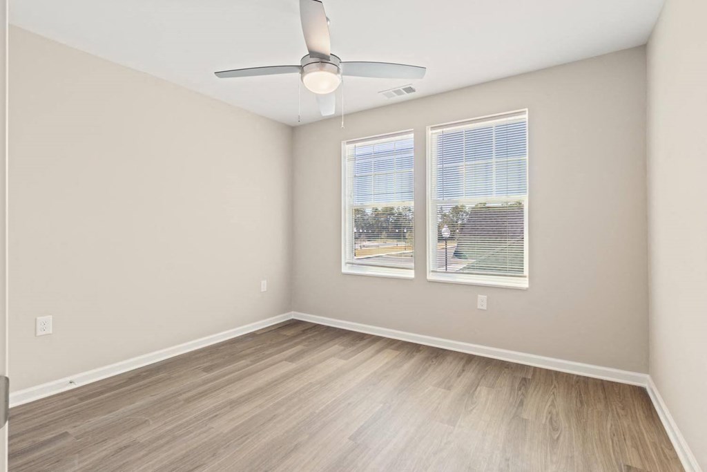 A room with a ceiling fan and two windows.