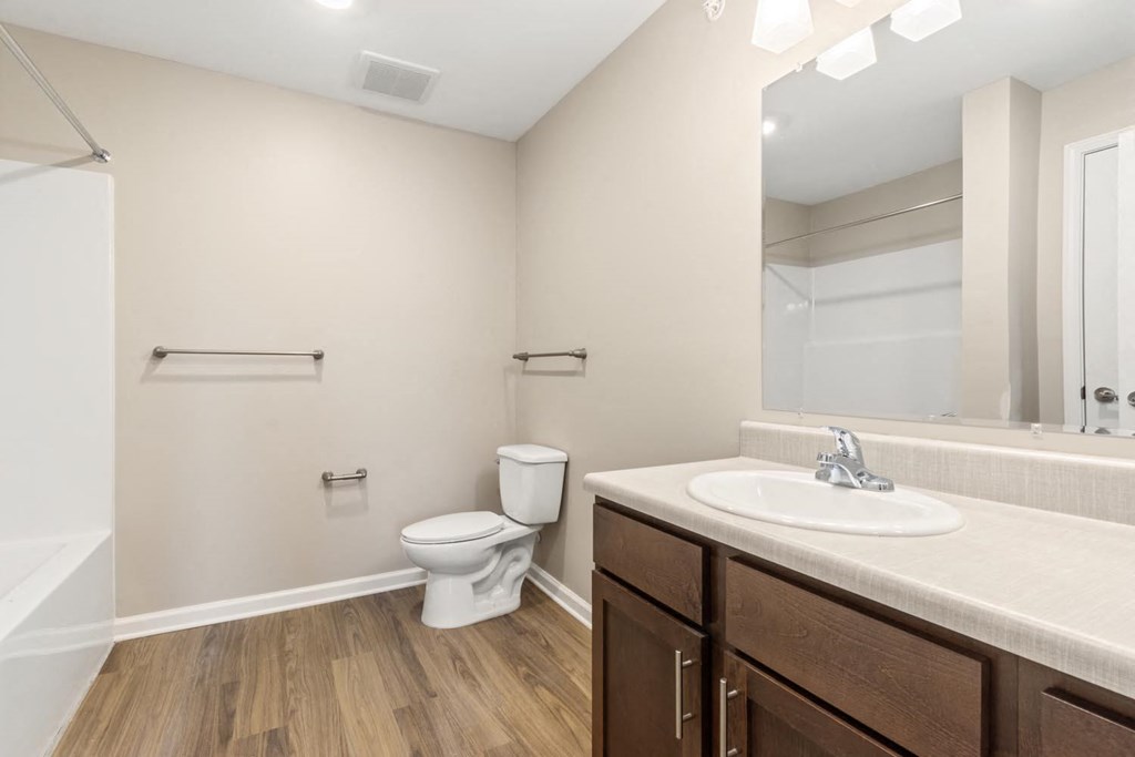 A white toilet sits in a bathroom with a wooden floor and a white sink.