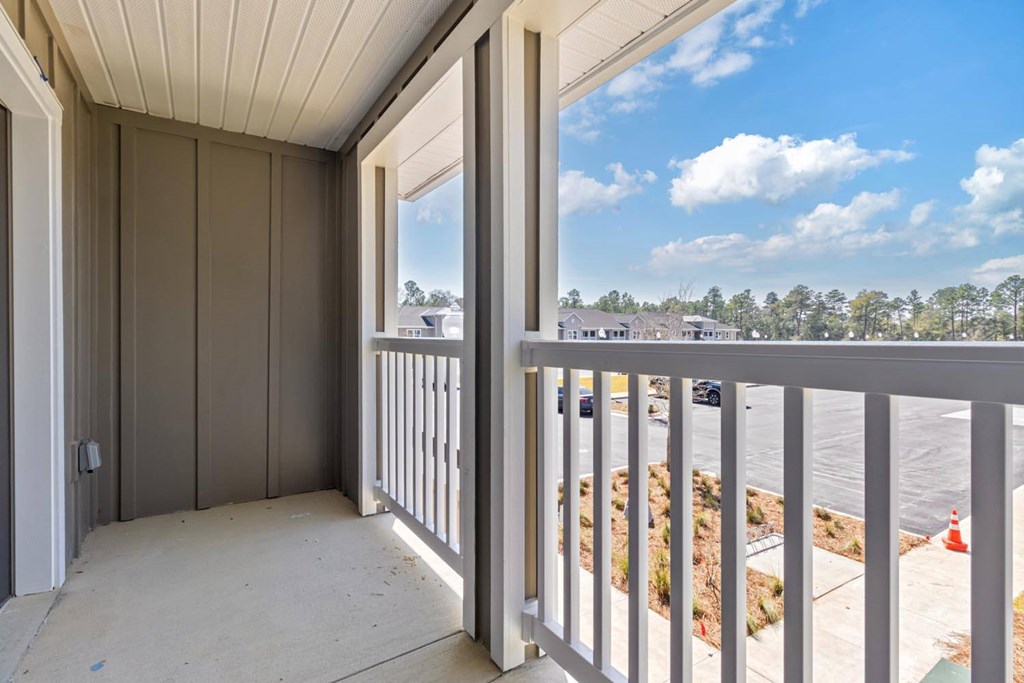 A balcony with a white railing and a view of a street with cars and houses.