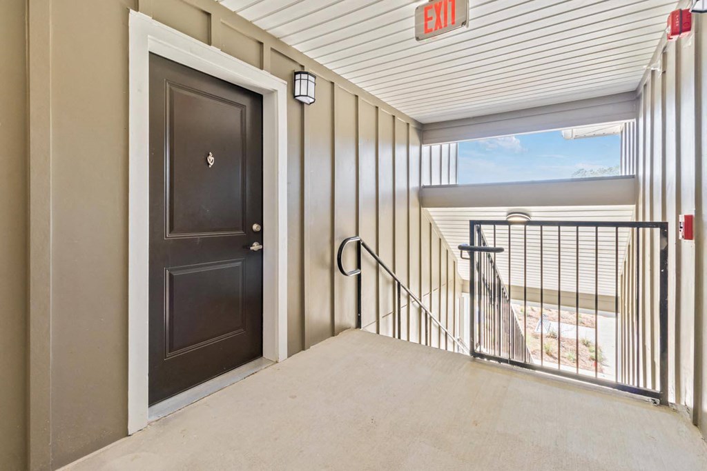 A brown door with a black handle is on the left and a metal railing is on the right.