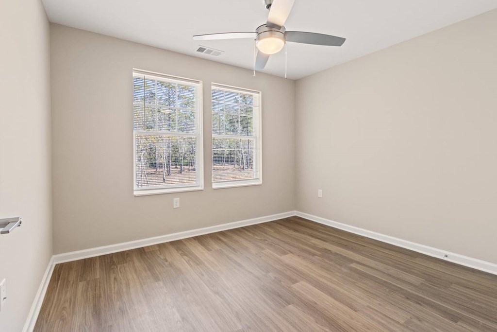 A room with a ceiling fan and two windows.