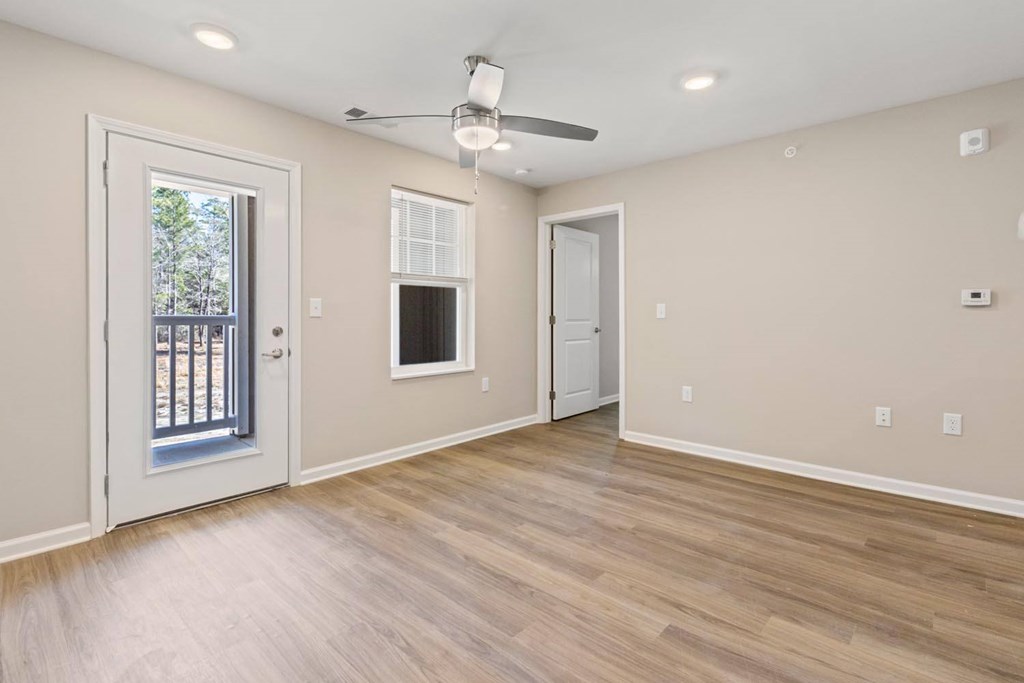 A room with a ceiling fan and light fixture, two doors, and a window with a view of a fence and trees.