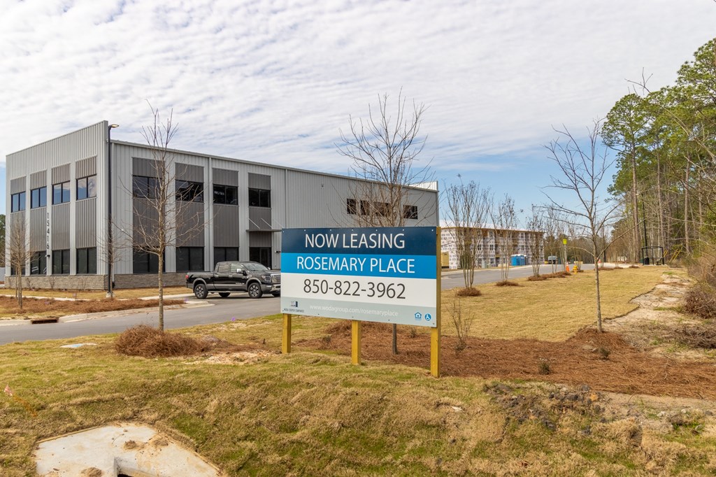 A sign in front of a building that says "Now Leasing Rosemary Place" with a phone number.