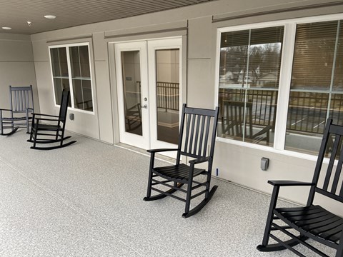 a group of rocking chairs on a porch with windows